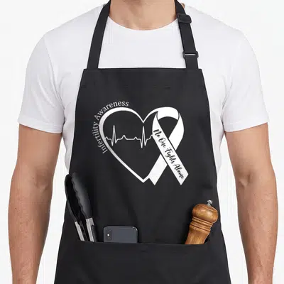 Infertility ribbon apron - White heart outline with heartbeat line and awareness ribbon containing text No One Fights — shown on a black cotton canvas apron against a white background