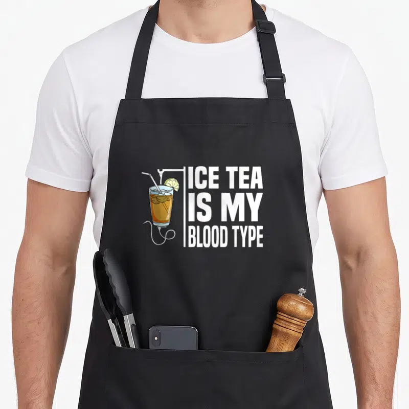 Tea nurse apron - Glass of iced tea with lemon and straw beside stacked text reading Ice Tea Is My Blood Type — shown on a black cotton canvas apron against a white background