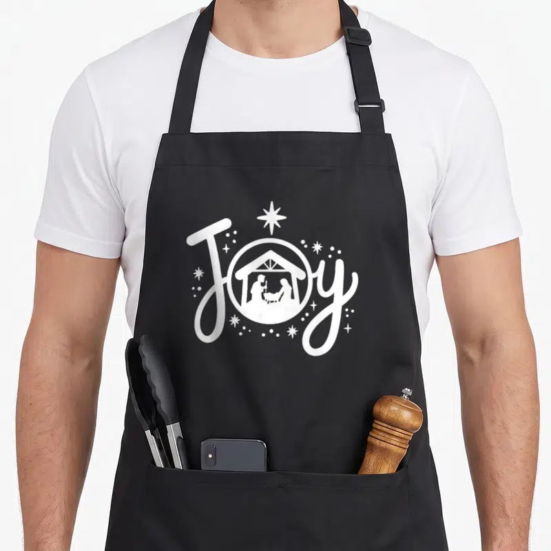 Christian family christmas aprons - White script JOY with circular nativity scene and star — shown on a black cotton canvas apron against a white background