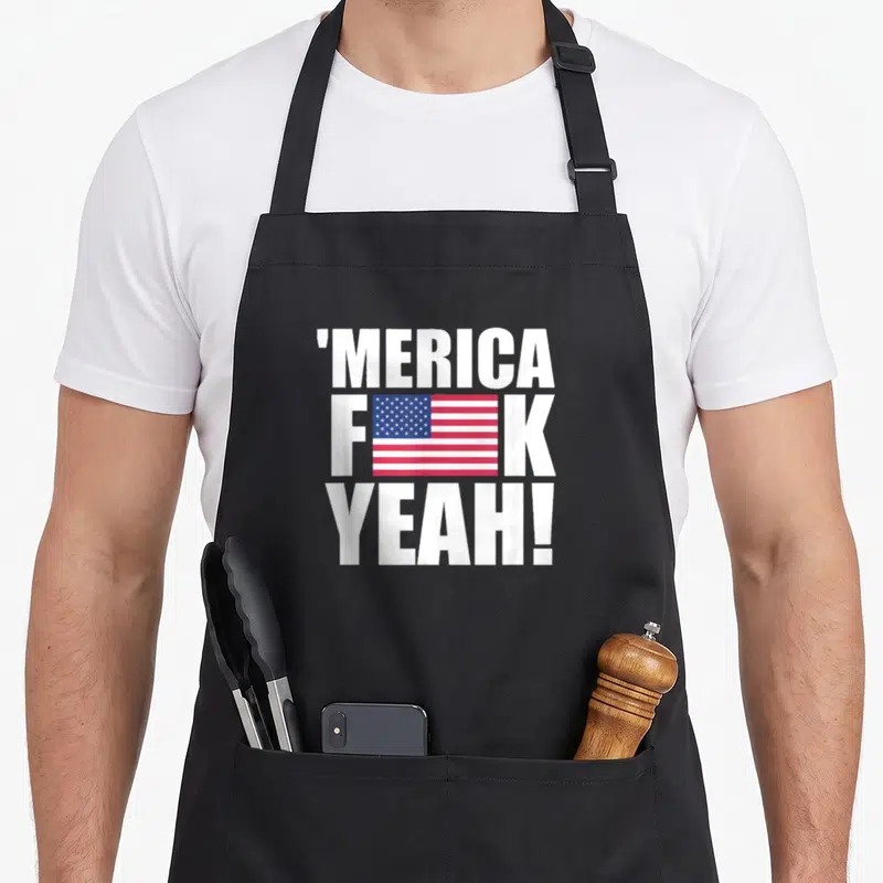 Yeah fourth of july aprons - Stacked white 'MERICA F K YEAH text with USA flag graphic replacing letter U — shown on a black cotton canvas apron against a white background