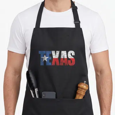 State texas apron - Distressed TEXAS text in blue white red with white star inside T — shown on a black cotton canvas apron against a white background