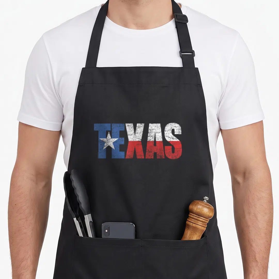 State texas apron - Distressed TEXAS text in blue white red with white star inside T — shown on a black cotton canvas apron against a white background