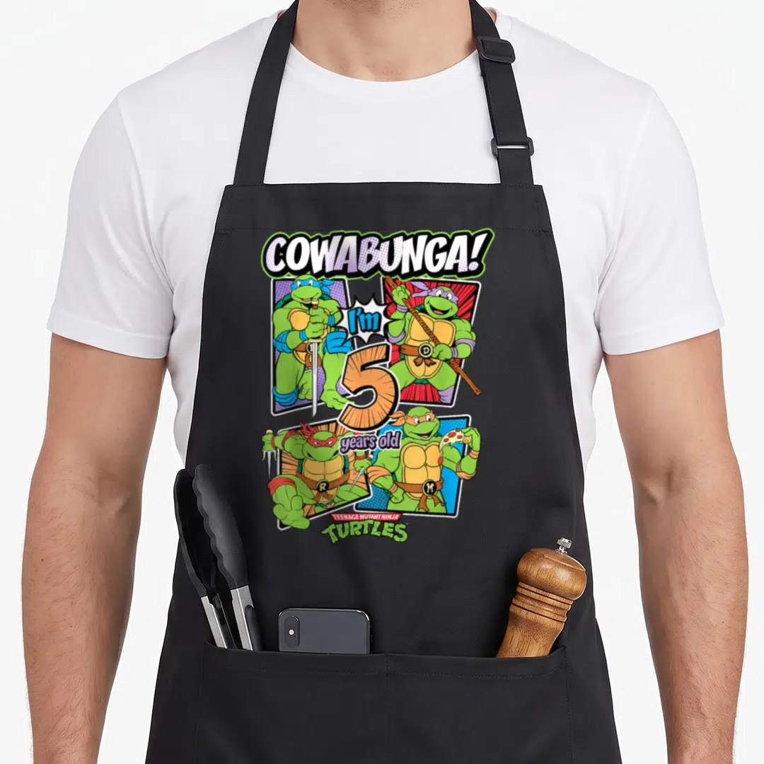 Funny cowabunga teenage cooking aprons - Four turtles surround orange number 5 with COWABUNGA text and TMNT logo — shown on a black cotton canvas apron against a white background