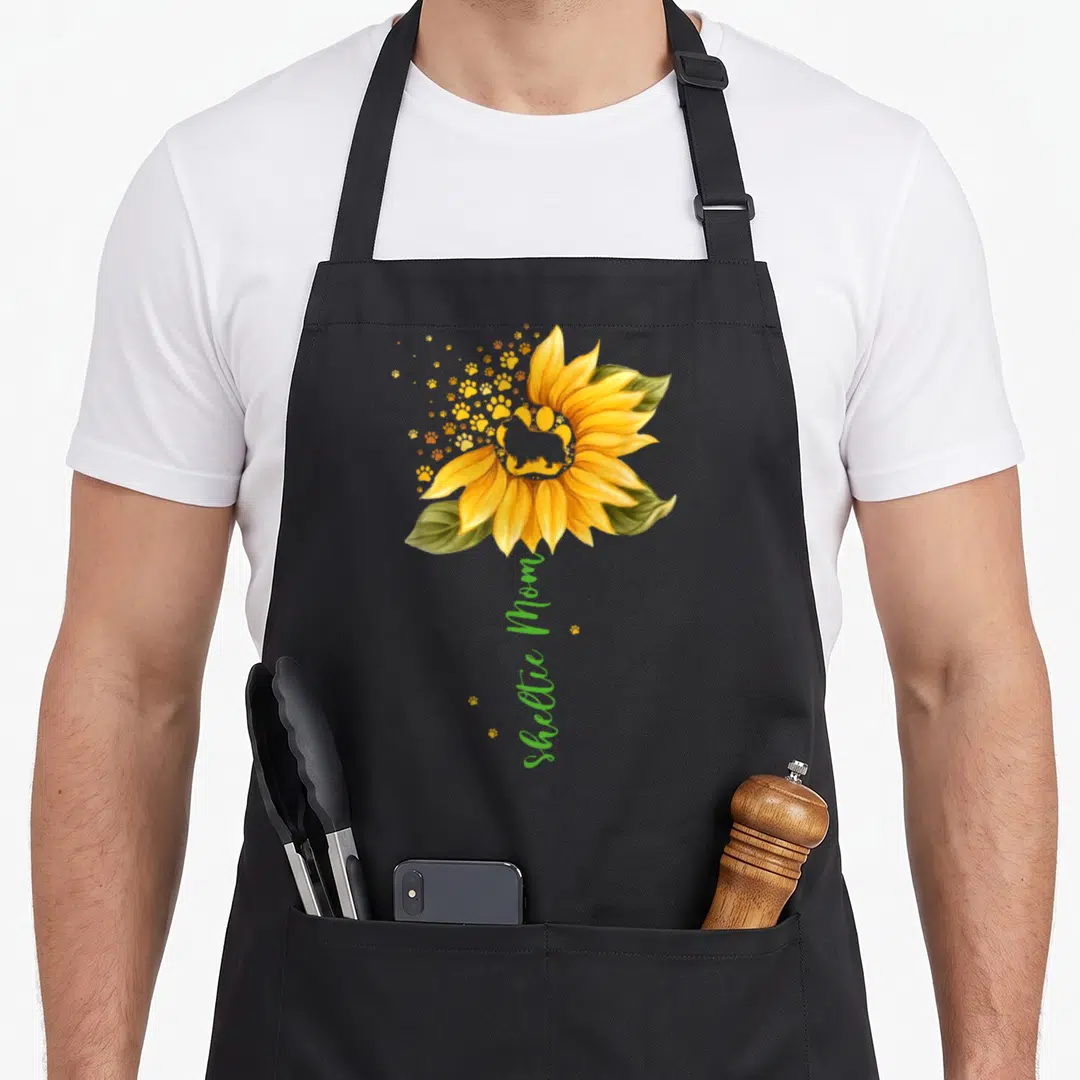 Sheltie sunflower dog apron - Sunflower with Sheltie silhouette and vertical Sheltie Mom text — shown on a black cotton canvas apron against a white background