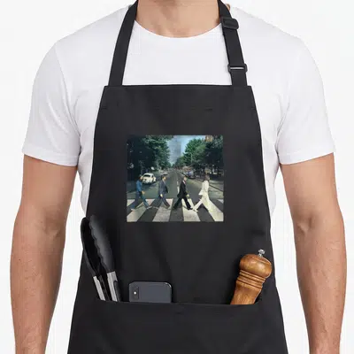 Crossing road apron - Four people walking across a zebra crosswalk in a city street photo — shown on a black cotton canvas apron against a white background