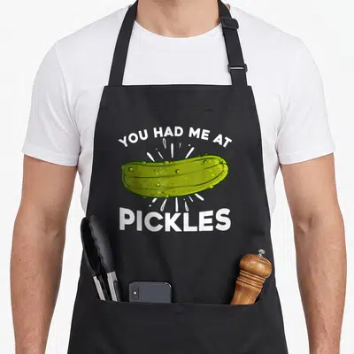 Pickled pickle apron - Green cartoon pickle between You Had Me At and Pickles text with white action lines — shown on a black cotton canvas apron against a white background