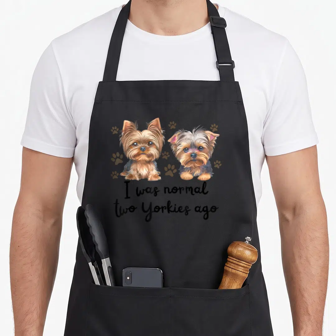 Normal yorkie apron - Two realistic Yorkies with scattered paw prints and text I was normal two Yorkies ago — shown on a black cotton canvas apron against a white background
