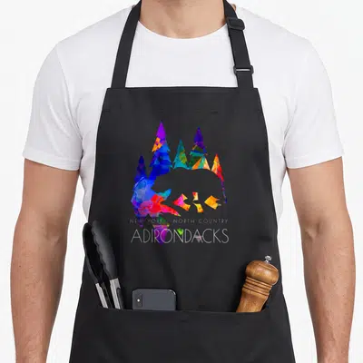 Bear new york apron - Geometric bear silhouette formed by blue purple red yellow and white pine trees with white text — shown on a black cotton canvas apron against a white background