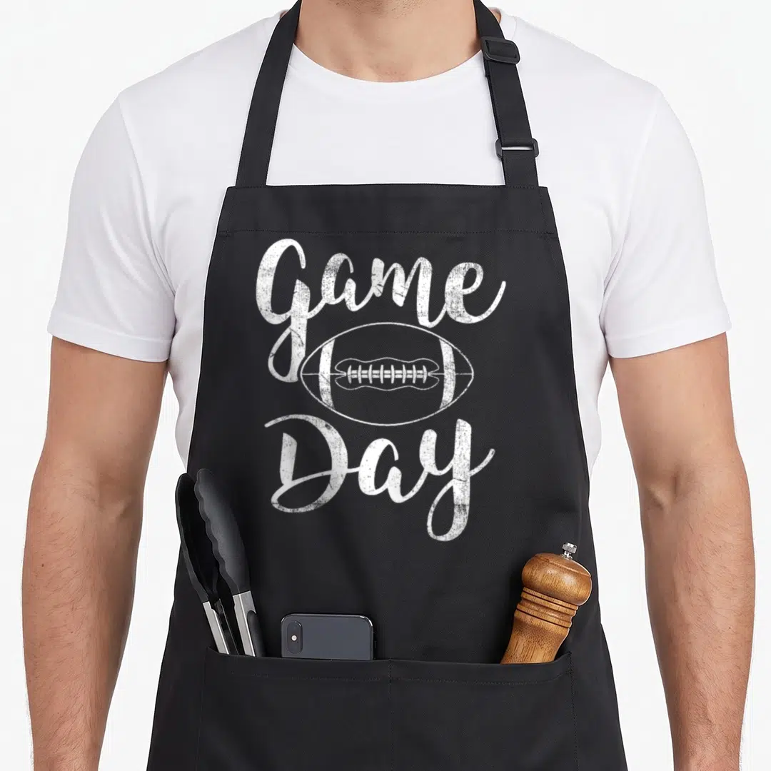 Funny game football apron - Distressed white Game Day text framing a line-art football illustration — shown on a black cotton canvas apron against a white background