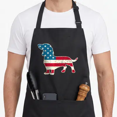 Dachshund 4th of july apron - Distressed American flag pattern filling a standing dachshund silhouette in blue red — shown on a black cotton canvas apron against a white background