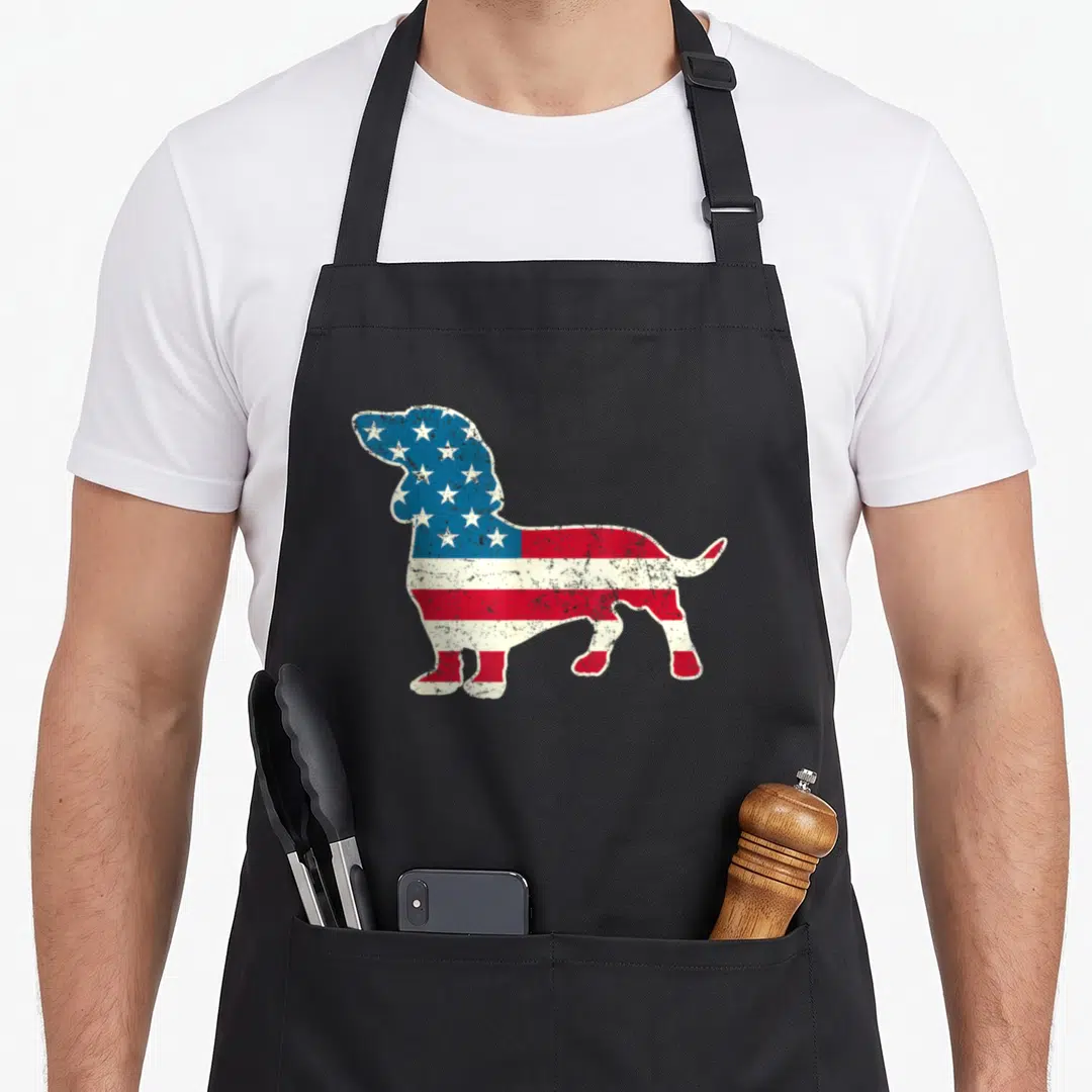 Dachshund 4th of july apron - Distressed American flag pattern filling a standing dachshund silhouette in blue red — shown on a black cotton canvas apron against a white background