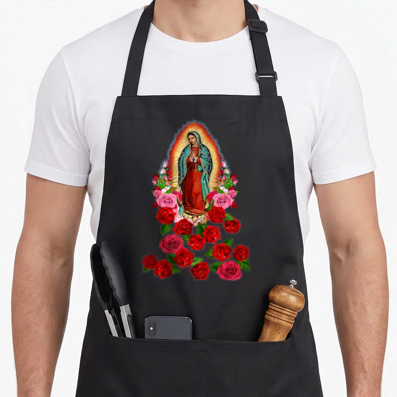 Funny our lady of guadalupe apron - Virgin Mary in golden halo surrounded by red and pink roses with small angel below — shown on a black cotton canvas apron against a white background