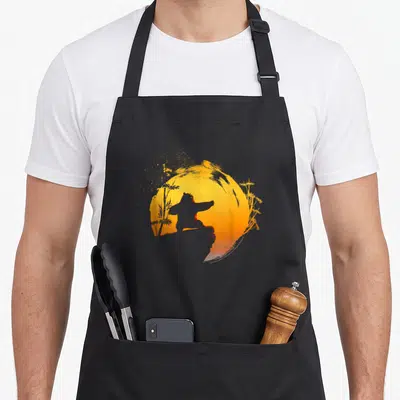 Tai kung apron - Panda silhouette in a martial arts pose against a yellow and orange brush-stroke sun with bamboo — shown on a black cotton canvas apron against a white background