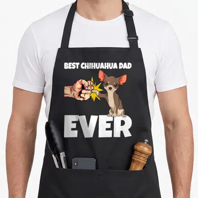Funny chihuahua dog dad apron - Cartoon chihuahua fist bumping human hand with best chihuahua dad ever text — shown on a black cotton canvas apron against a white background