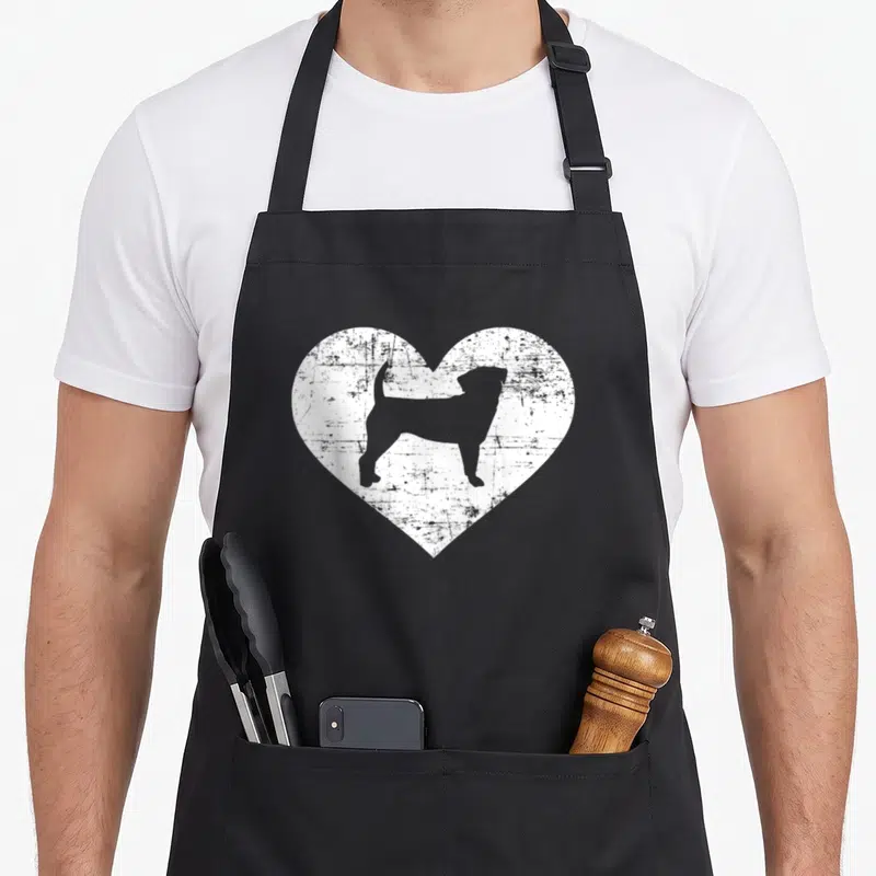 Funny puggle apron - Grey dog silhouette inside a white distressed heart graphic — shown on a black cotton canvas apron against a white background