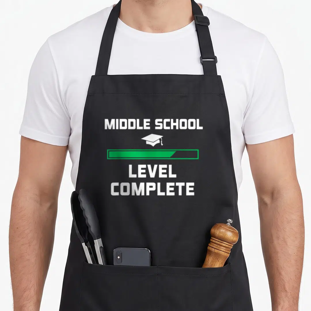 Middle grade graduation apron - White cap and green progress bar with MIDDLE SCHOOL LEVEL COMPLETE text — shown on a black cotton canvas apron against a white background
