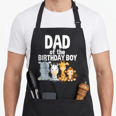 Jungle safari birthday apron - Dad of the Birthday Boy text above cartoon hippo zebra giraffe and monkey — shown on a black cotton canvas apron against a white background