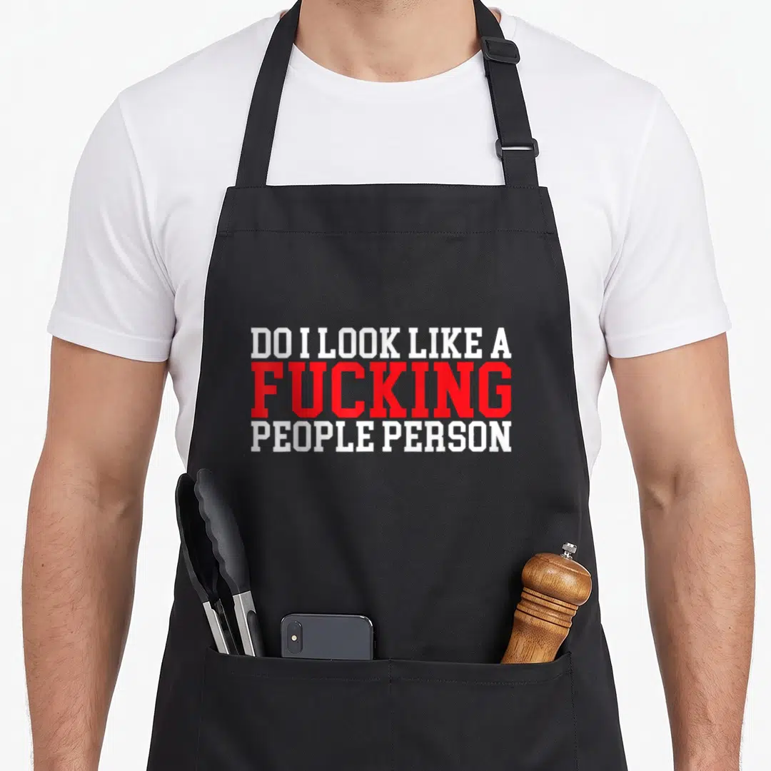 Funny sarcasm apron - White and red stacked text reading DO I LOOK LIKE A FUCKING PEOPLE PERSON — shown on a black cotton canvas apron against a white background
