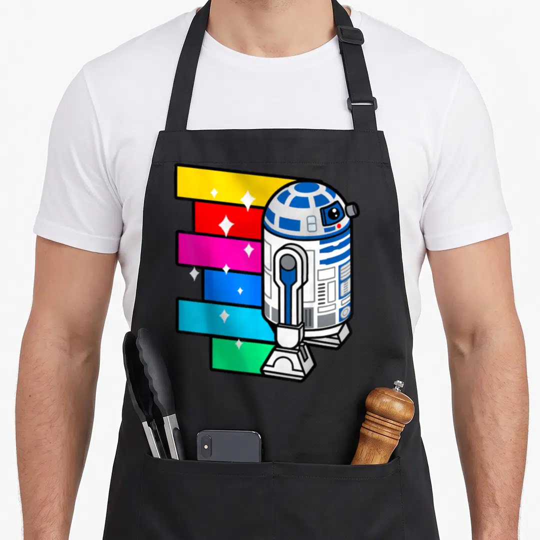 Rainbow cartoon apron - Cartoon R2-D2 robot beside six colorful stripes with white stars on black fabric — shown on a black cotton canvas apron against a white background
