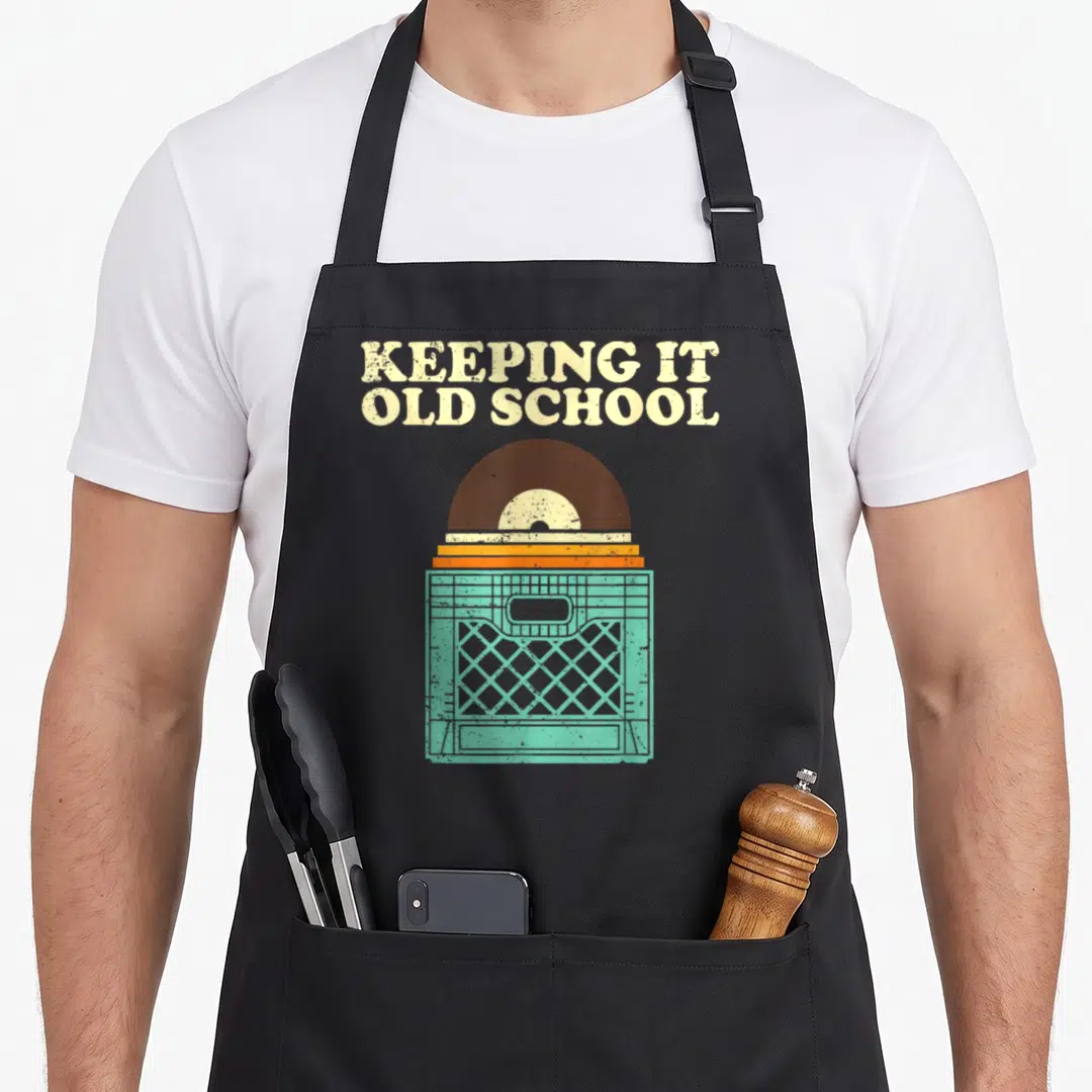 Album vinyl apron - KEEPING IT OLD SCHOOL text above brown record on mint green crate — shown on a black cotton canvas apron against a white background
