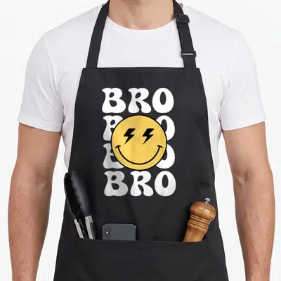 Bro custom face apron - Yellow smiley face with black lightning eyes over four stacked white BRO words on black fabric — shown on a black cotton canvas apron against a white background