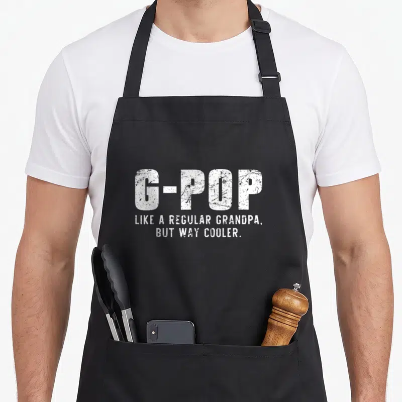 Way grandpa apron - White distressed typography reading G-Pop Like A Regular Grandpa But Way Cooler on black fabric — shown on a black cotton canvas apron against a white background