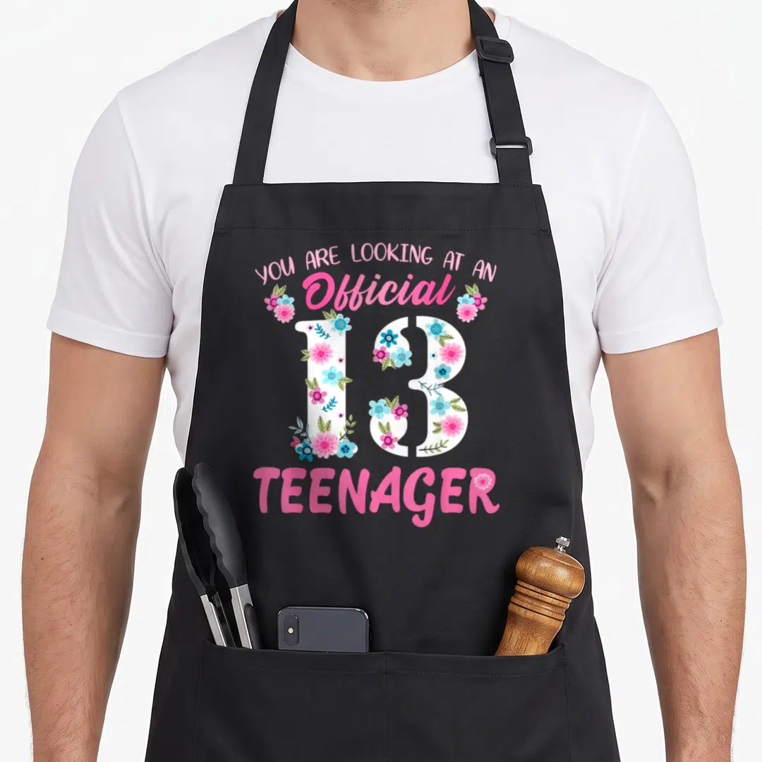 Flower birthday apron - Official 13 Teenager text with floral filled number 13 in pink and blue — shown on a black cotton canvas apron against a white background