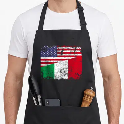 Italy american flag apron - Distressed graphic of USA flag blending into Italian flag with red white blue and green — shown on a black cotton canvas apron against a white background