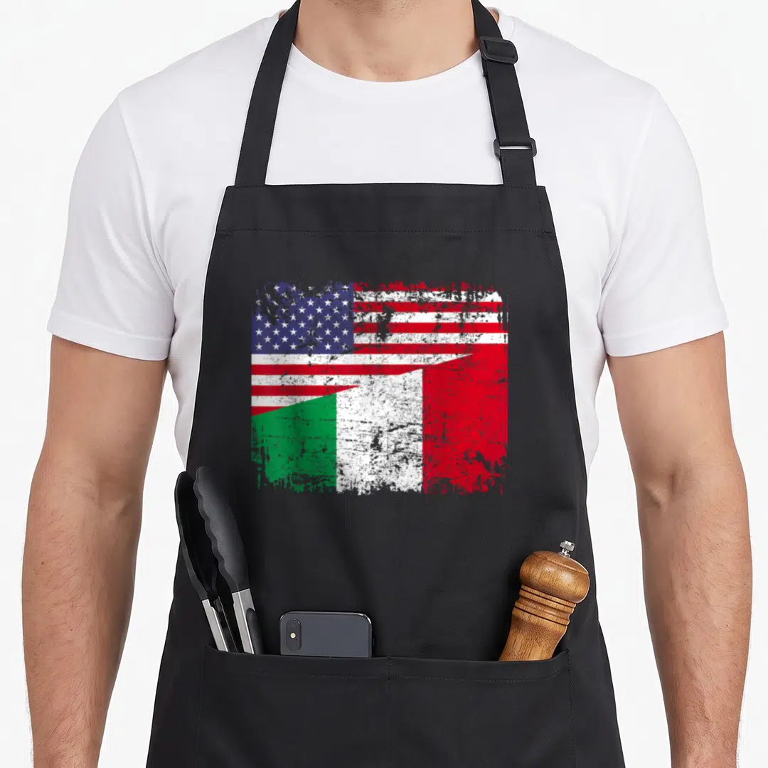 Italy american flag apron - Distressed graphic of USA flag blending into Italian flag with red white blue and green — shown on a black cotton canvas apron against a white background