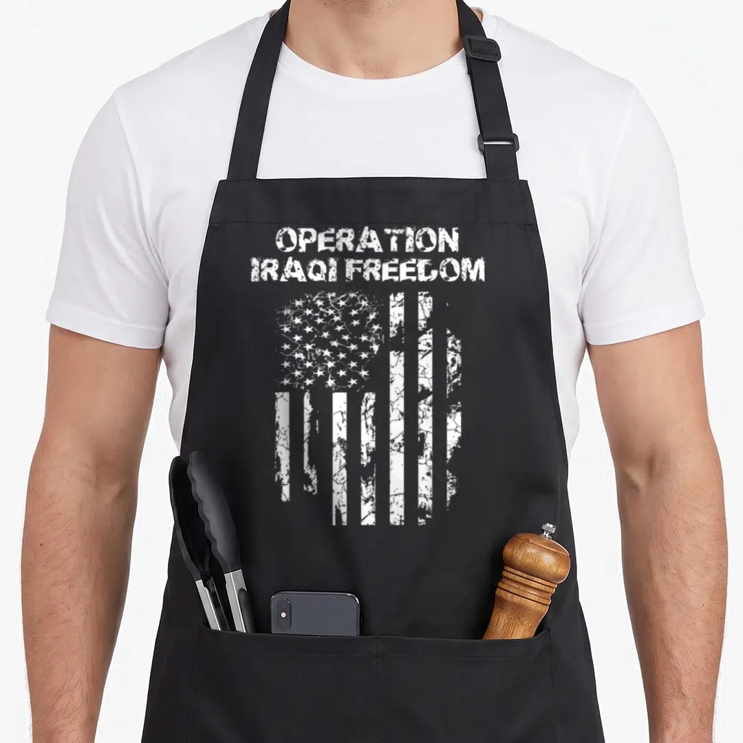 Operation combat apron - Distressed white USA flag below stacked text reading Operation Iraqi Freedom — shown on a black cotton canvas apron against a white background