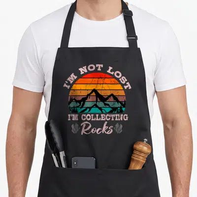 Lost erosion apron - Striped sun mountains text I'm Not Lost Collecting Rocks two crystals — shown on a black cotton canvas apron against a white background