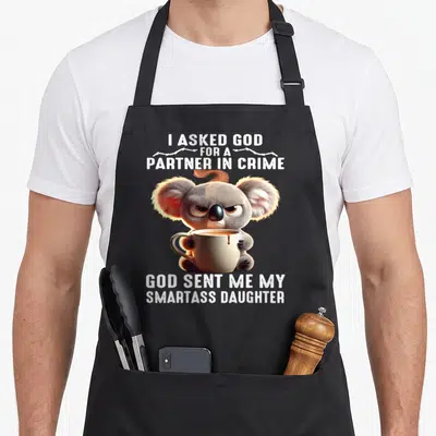 Partner mom daughter apron - Grumpy koala holding coffee cup with barbed wire and sarcastic text about smartass daughter — shown on a black cotton canvas apron against a white background