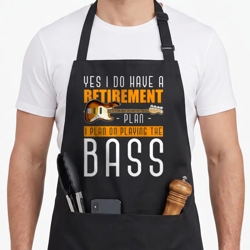 Bass retirement apron - Horizontal sunburst bass guitar over stacked white and orange text reading Yes I Do Have — shown on a black cotton canvas apron against a white background