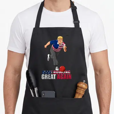 Trump bowling apron - Cartoon man bowling with red ball and stacked patriotic text below — shown on a black cotton canvas apron against a white background