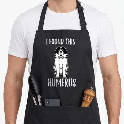 Pet owner dog apron - Saint Bernard holding bone with text I FOUND THIS HUMERUS — shown on a black cotton canvas apron against a white background