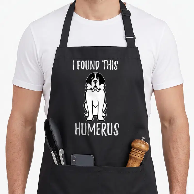 Pet owner dog apron - Saint Bernard holding bone with text I FOUND THIS HUMERUS — shown on a black cotton canvas apron against a white background