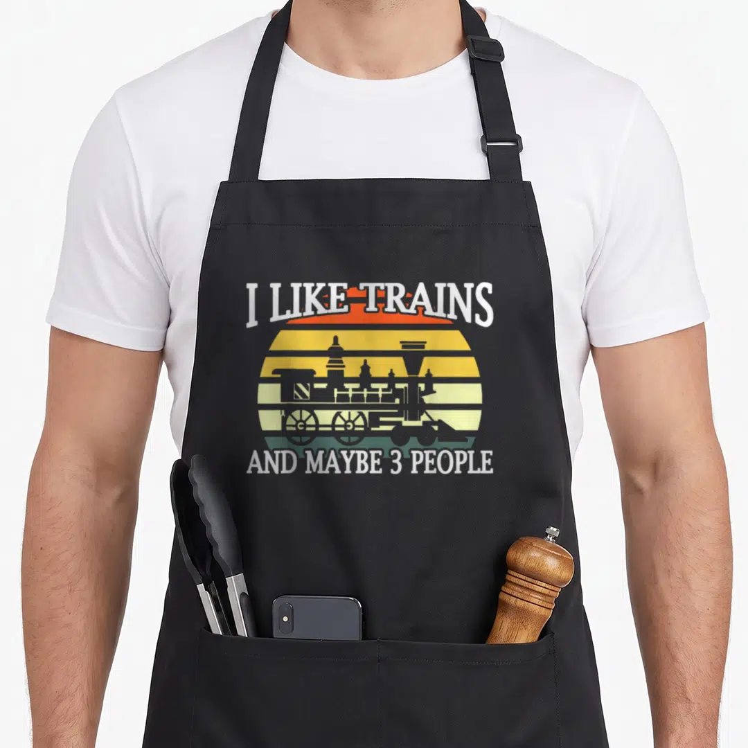 Railroad grandpa apron - Grey steam train silhouette on retro striped sun with text I LIKE TRAINS AND MAYBE 3 PEOPLE — shown on a black cotton canvas apron against a white background