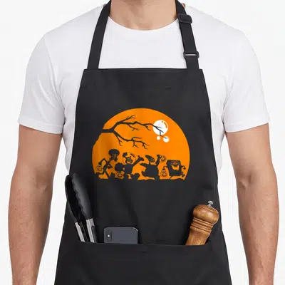 Squarepant shot halloween apron - Grey character silhouettes holding pumpkins against an orange moon and white moon — shown on a black cotton canvas apron against a white background