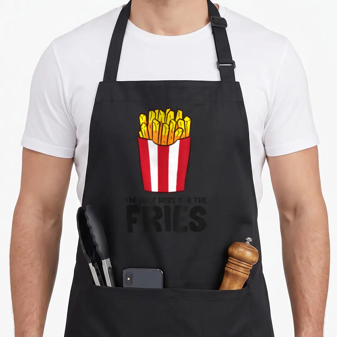 Pomme french apron - Cartoon yellow french fries in red and white striped container with black text below — shown on a black cotton canvas apron against a white background