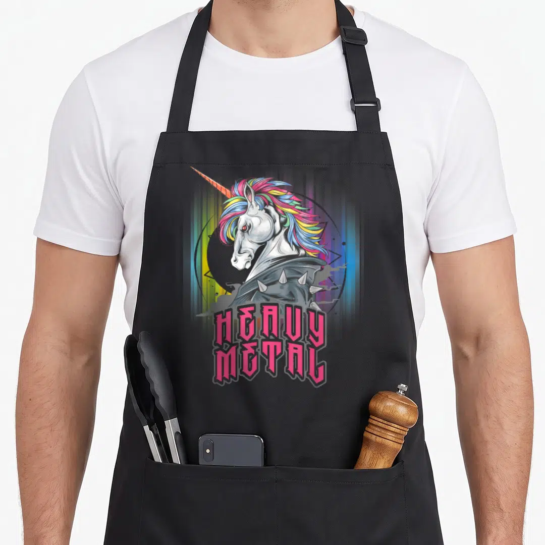 Unicorn heavy apron - Cartoon unicorn with spiked collar and pink heavy metal text — shown on a black cotton canvas apron against a white background