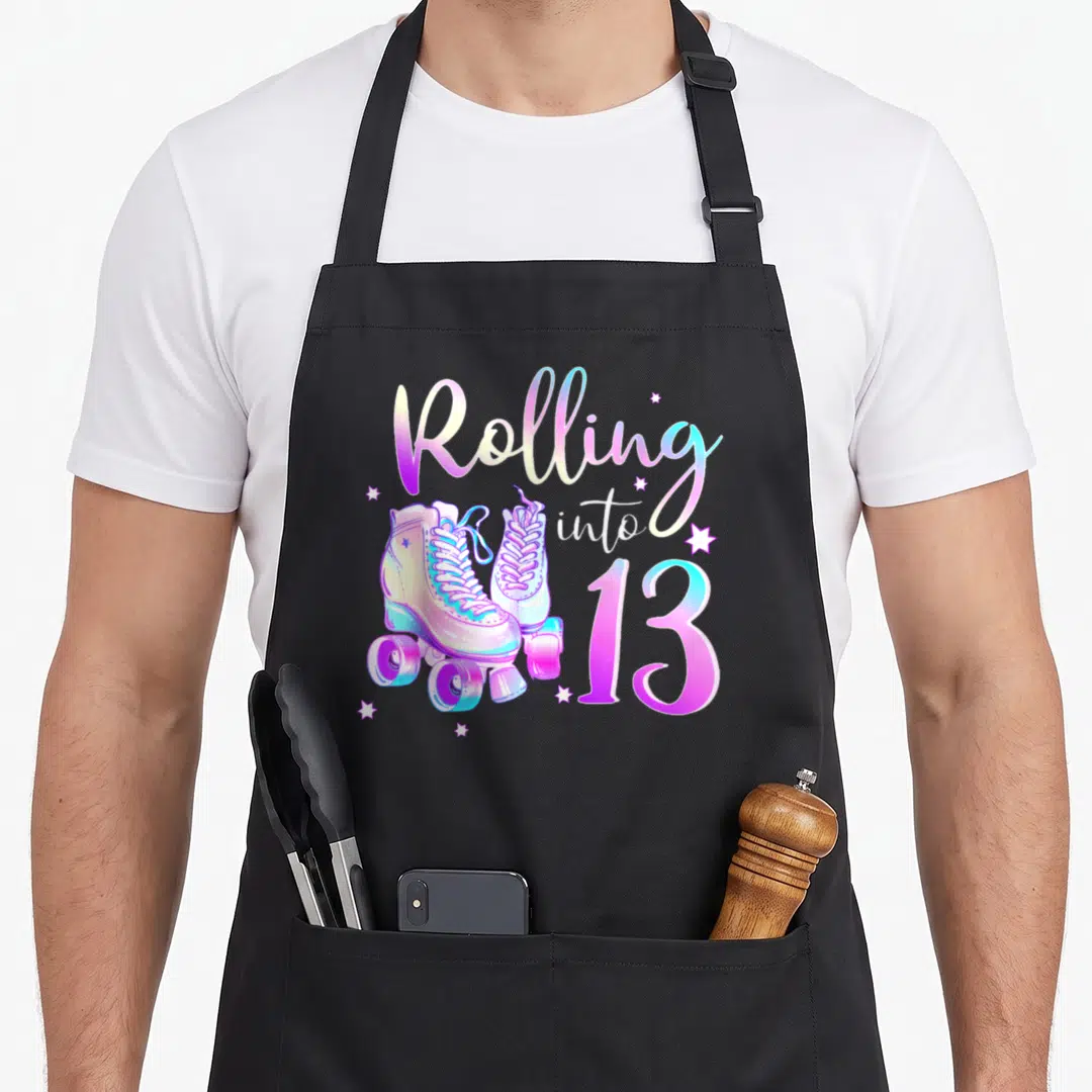 Rolling 13th birthday apron - Rolling into 13 text with roller skates and stars in purple blue yellow white — shown on a black cotton canvas apron against a white background