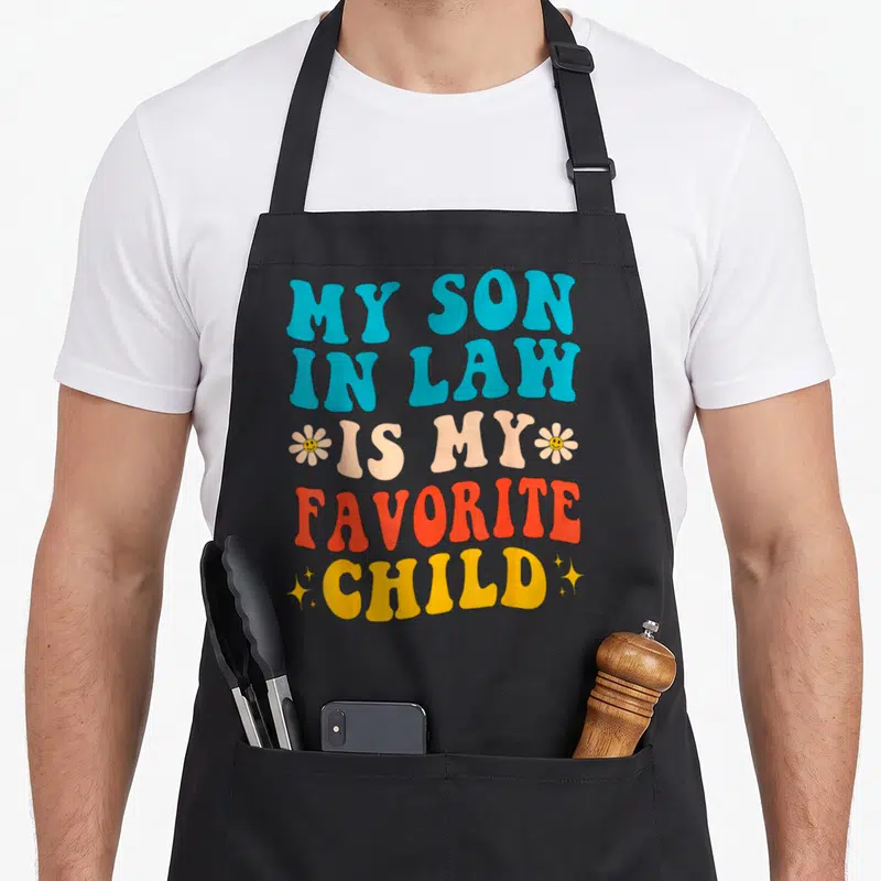 Retro law mother son aprons - Retro text MY SON IN LAW IS MY FAVORITE CHILD with smiley flowers and stars in blue peach — shown on a black cotton canvas apron against a white background