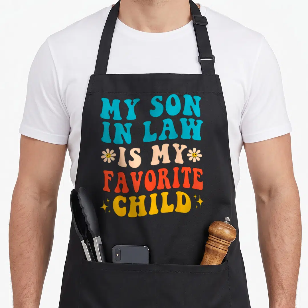 Retro law mother son aprons - Retro text MY SON IN LAW IS MY FAVORITE CHILD with smiley flowers and stars in blue peach — shown on a black cotton canvas apron against a white background