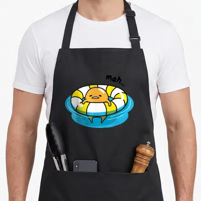 Pool gudetama apron - Lazy orange egg in yellow white ring floating on blue water with meh text — shown on a black cotton canvas apron against a white background