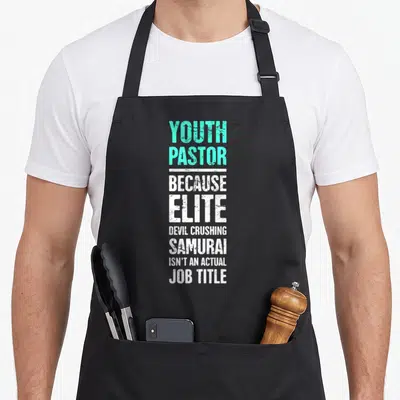 Funny youth pastor apron - Mint green and white stacked text reading Youth Pastor Because Elite Devil Crushing Samurai — shown on a black cotton canvas apron against a white background