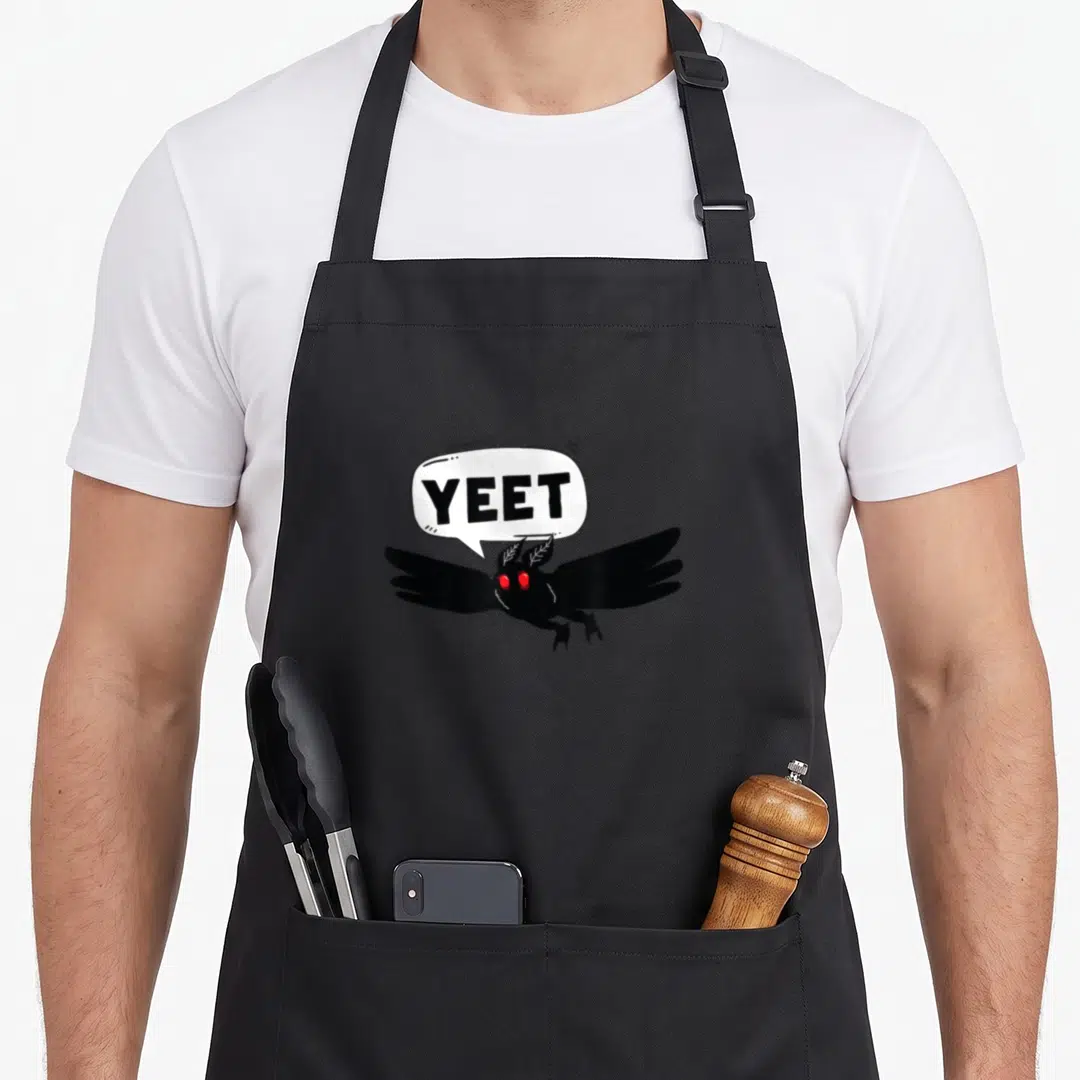 Mothman halloween birthday apron - Cartoon black moth with red eyes and white speech bubble reading yeet — shown on a black cotton canvas apron against a white background