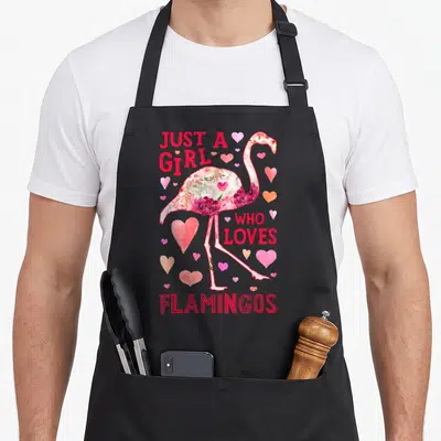 Flamingo the floral apron - Flamingo silhouette filled with pink and white flowers surrounded by hearts and red text — shown on a black cotton canvas apron against a white background