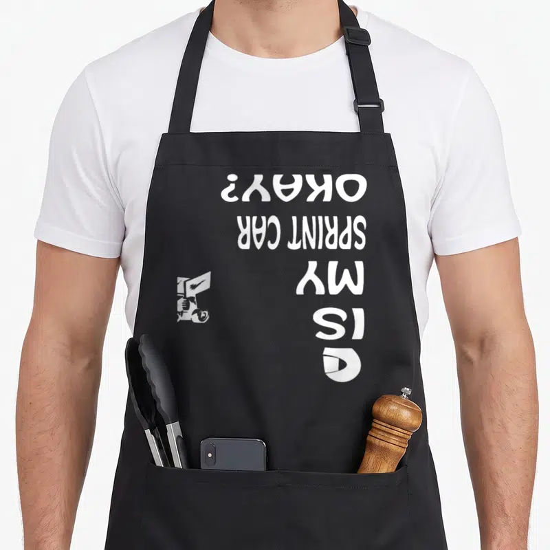 Midget track apron - White sprint car silhouette and stacked text reading IS MY SPRINT CAR OKAY? rotated 90 degrees — shown on a black cotton canvas apron against a white background