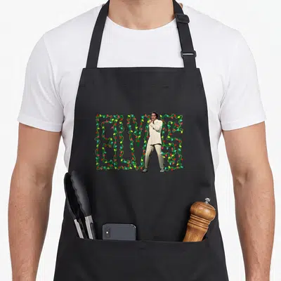 Elvis christmas lights apron - Photo of Elvis Presley in white suit standing before green ELVIS letters wrapped in red — shown on a black cotton canvas apron against a white background
