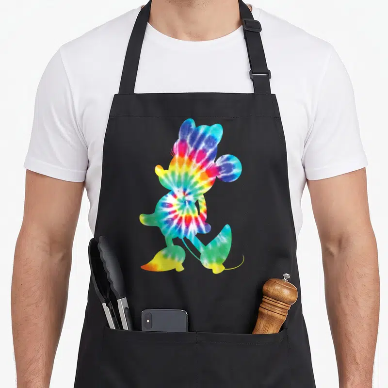 90s tie dye apron - Walking mouse silhouette filled with red yellow green blue purple tie dye pattern — shown on a black cotton canvas apron against a white background